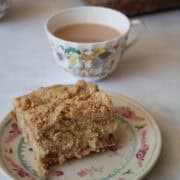 A cup of tea next to a slice of rhubarb crumb cake on a plate.