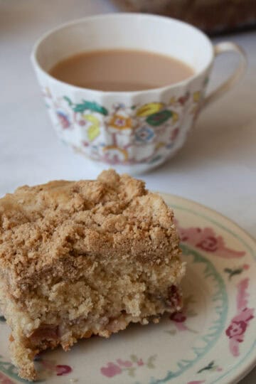 A cup of tea next to a slice of rhubarb crumb cake on a plate.