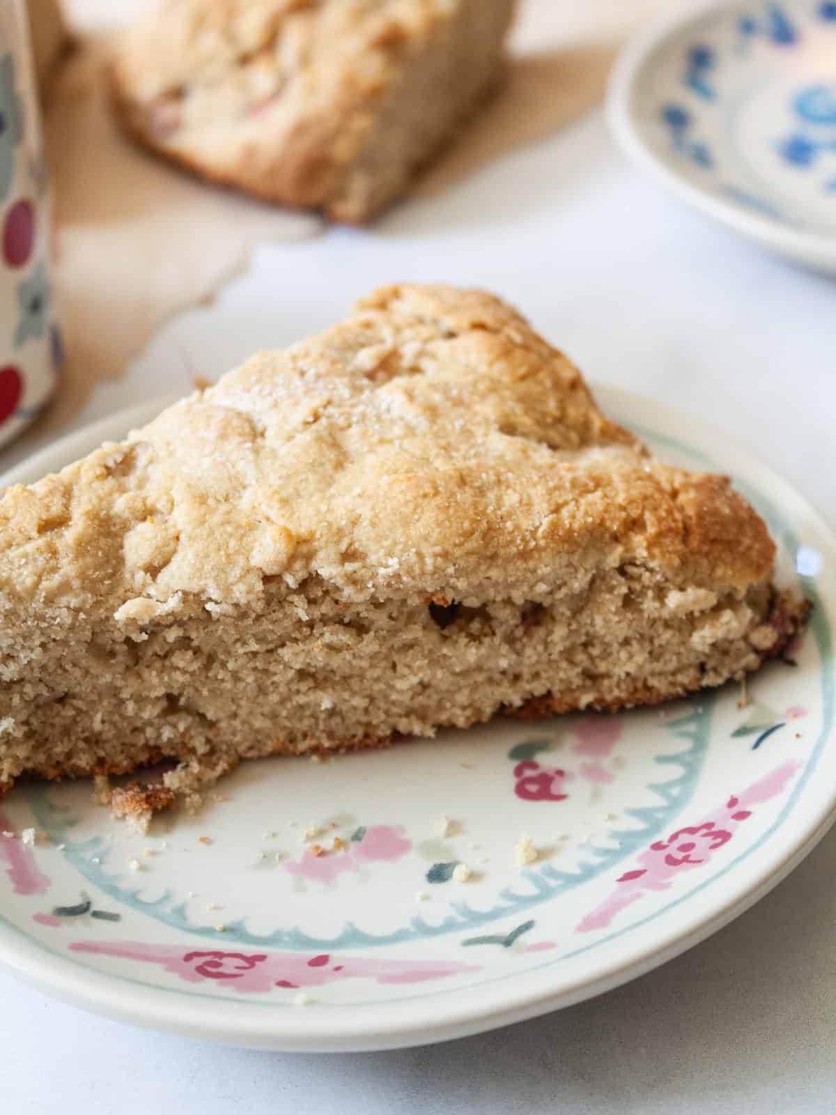 Tender and flaky whole grain strawberry rhubarb scones are a perfect summer morning treat. Make these with whole wheat or gf oat flour. A strawberry rhubarb scone on a plate.