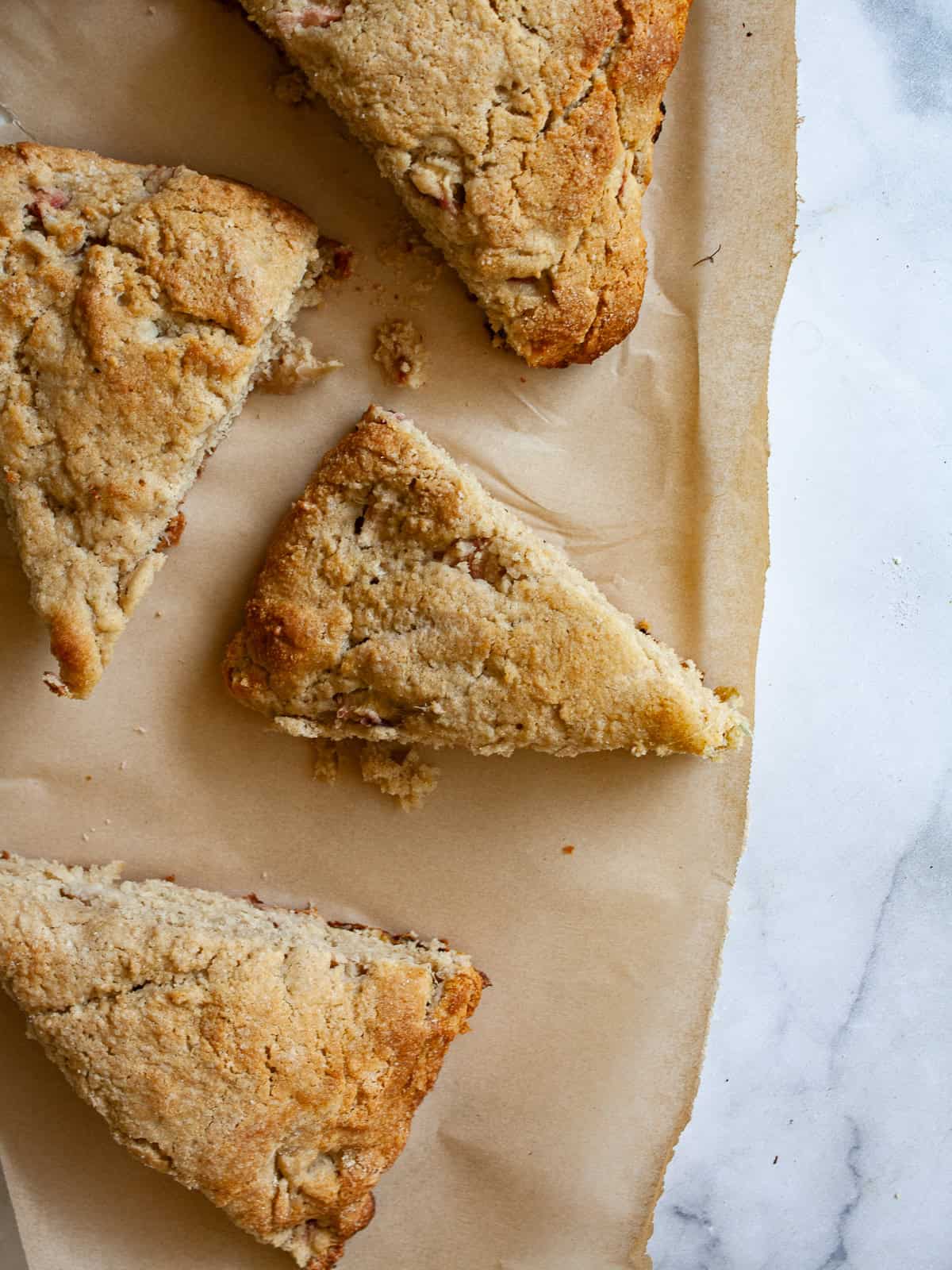 Tender and flaky whole grain strawberry rhubarb scones are a perfect summer morning treat. Make these with whole wheat or gf oat flour. Strawberry rhubarb scones on a piece of parchment paper.