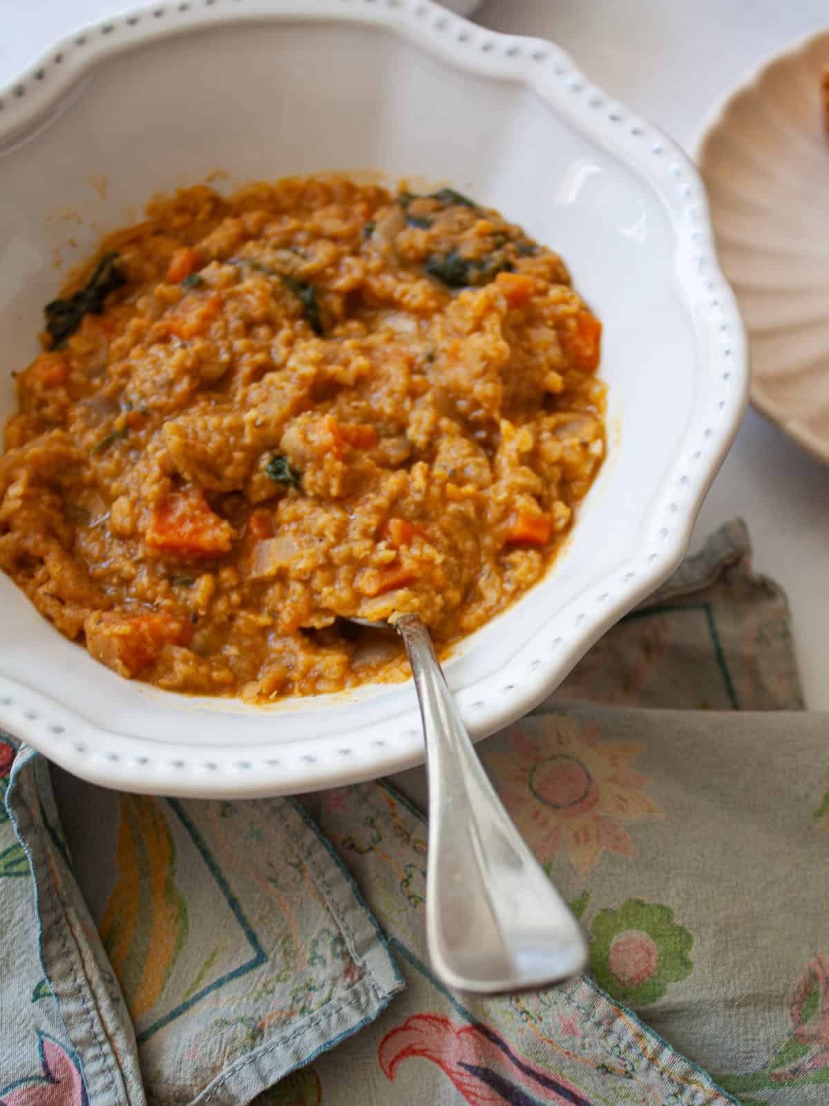 A hearty vegetarian red lentil stew that's packed with vegetables to make a satisfying dinner. Easy to adapt and make-ahead friendly. A bowl of red lentil stew with a spoon in it.