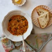 A bowl of red lentil stew, bread, and lemon wedges.