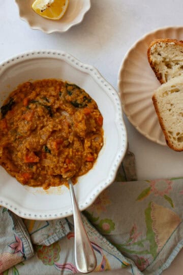 A bowl of red lentil stew, bread, and lemon wedges.