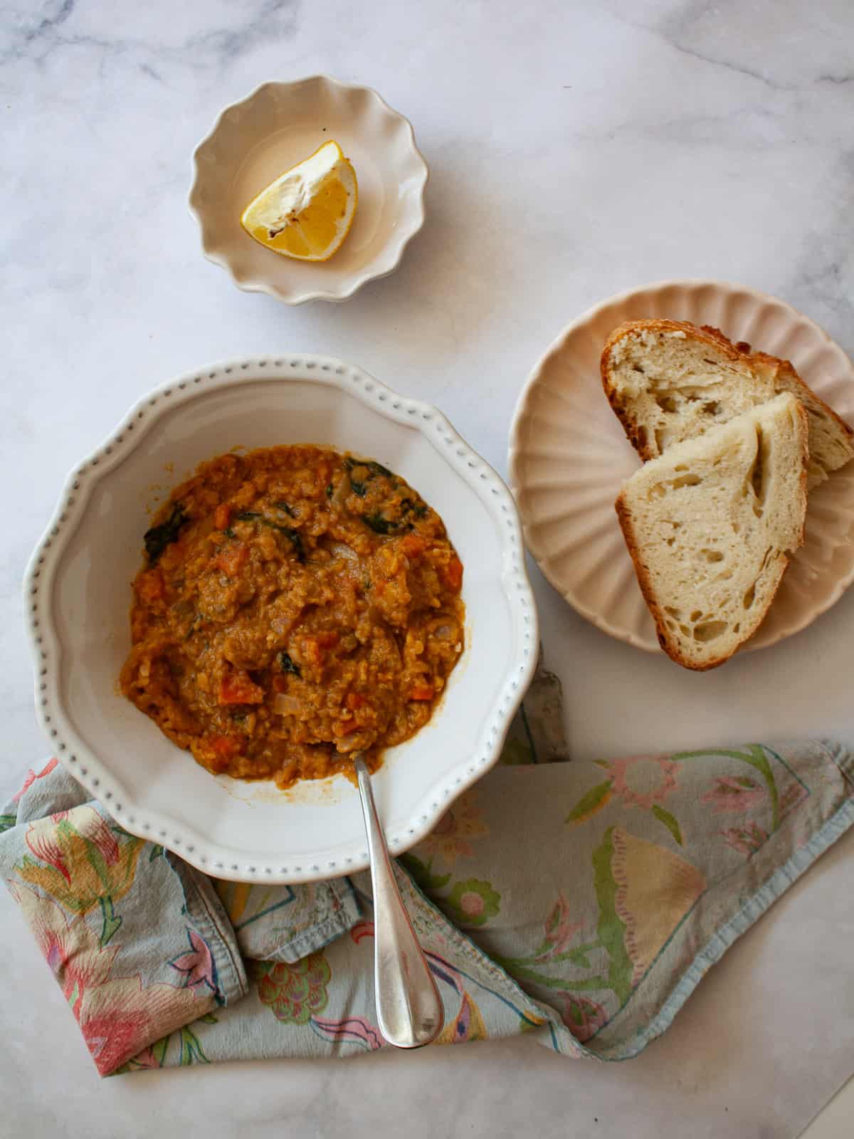 A hearty vegetarian red lentil stew that's packed with vegetables to make a satisfying dinner. Easy to adapt and make-ahead friendly. A bowl of red lentil stew, bread, and lemon wedges.