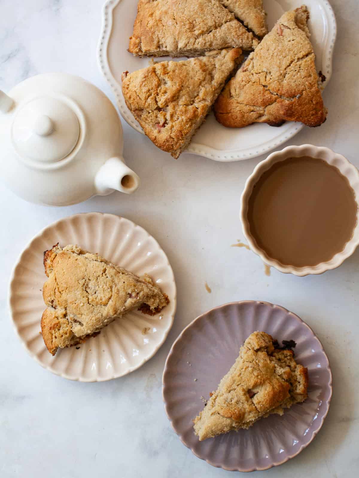 A plate of whole wheat rhubarb scones, a tea pot, and scones on plates.