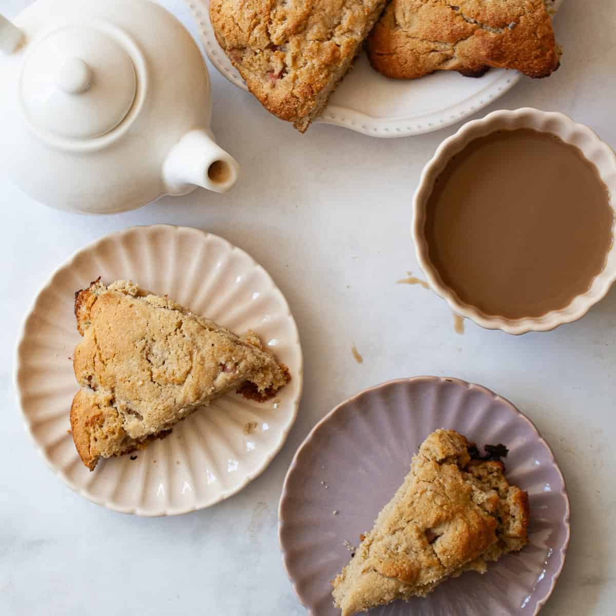 A tea pot and a cup of tea next to whole wheat rhubarb scones.