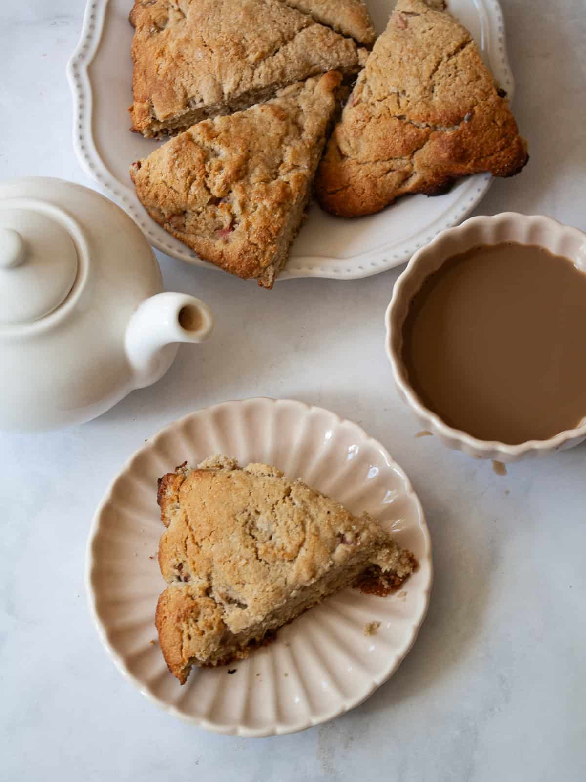 Tender, flaky rhubarb scones made with whole wheat flour and lots of tart spring rhubarb and a hint of orange zest. A whole wheat rhubarb scone on a plate next to tea.