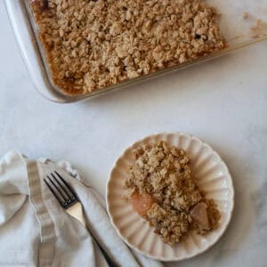 A napkin and fork next to a plate with rhubarb apple crisp, and a pan of crisp next to it.