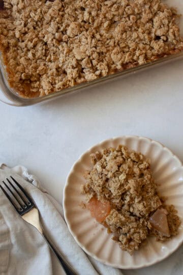 A napkin and fork next to a plate with rhubarb apple crisp, and a pan of crisp next to it.