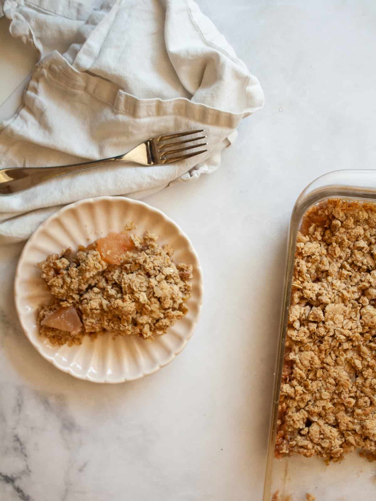 A jammy apple rhubarb crisp pairs seasonal rhubarb with sweet apples. Make the buttery oat topping gluten-free or use whole wheat flour. A piece of apple rhubarb crisp on a plate next to the pan of crisp.