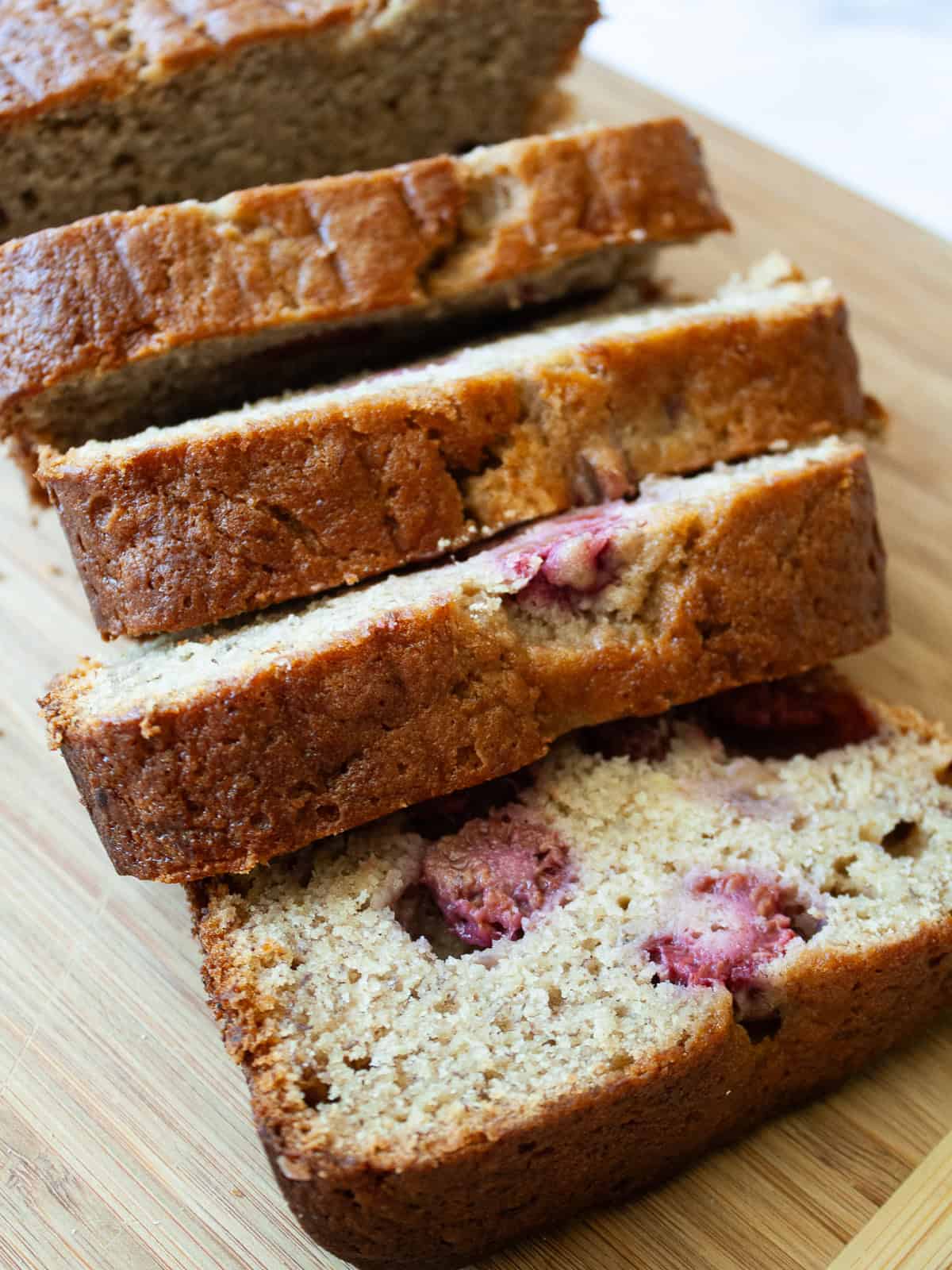 An uptick on a classic, this whole-grain raspberry banana bread features a soft, tender bread studded with juicy pockets of raspberries. Raspberries peek out of slices of banana raspberry bread.