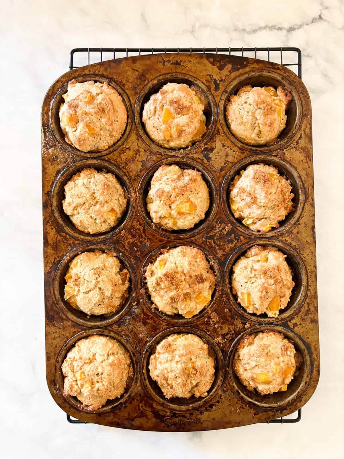 Yogurt, whole grains, and juicy peaches are swirled together with brown sugar in these tender and good-for-you gluten free peach muffins. A baked tin of gluten free peach muffins.