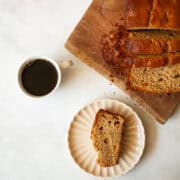 A cup of coffee next to a loaf of gluten free peach quick bread and a slice of bread.