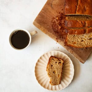 A cup of coffee next to a loaf of gluten free peach quick bread and a slice of bread.