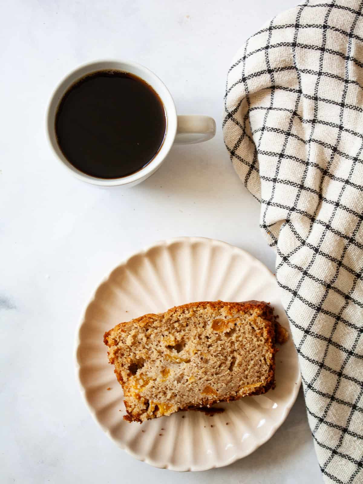 Juicy fresh peaches infuse this gluten-free peach quick bread with sweet summer flavor! Made with whole-grain oat flour and fresh fruit. A slice of gluten free peach quick bread on a plate.