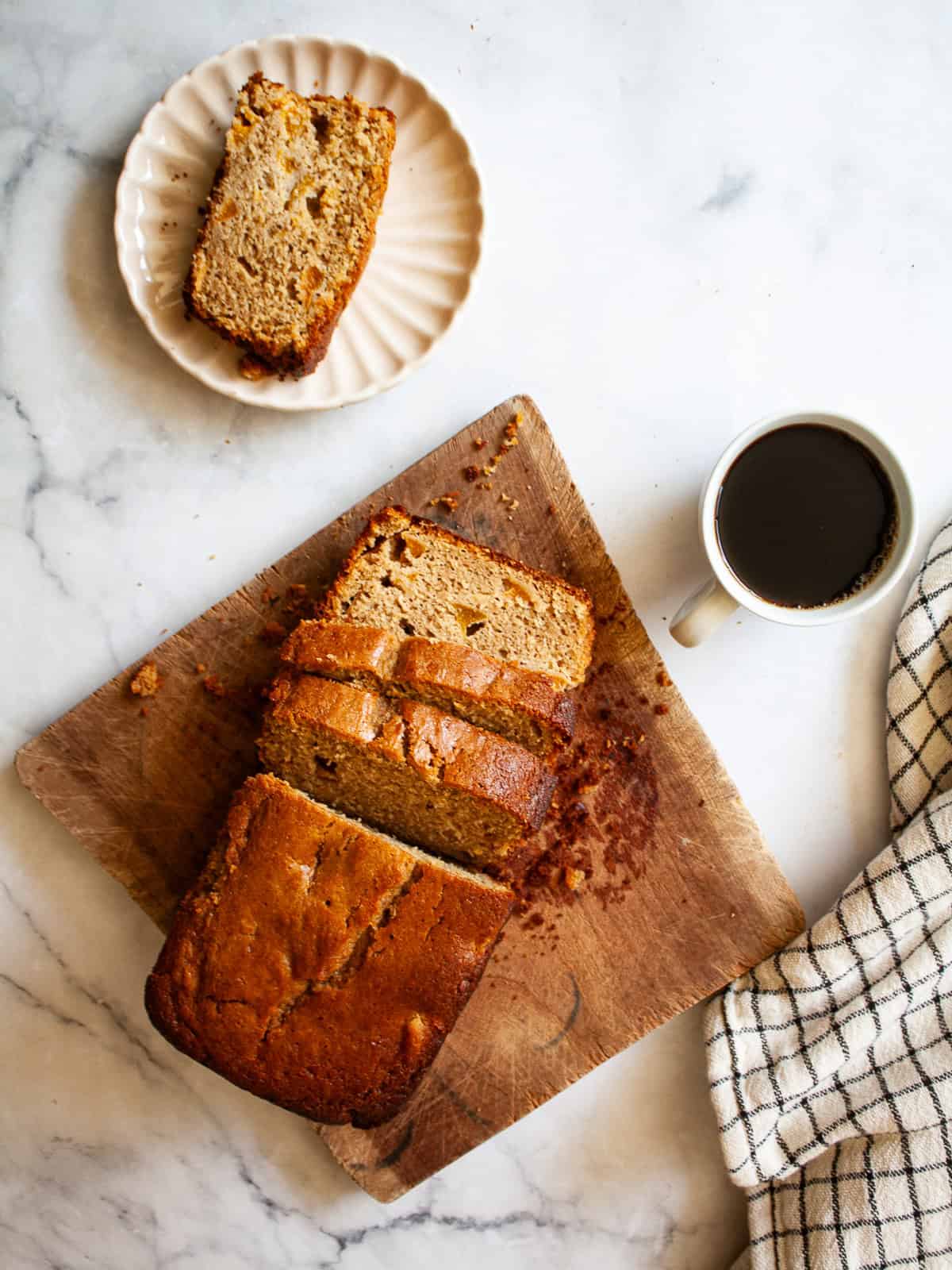 Juicy fresh peaches infuse this gluten-free peach quick bread with sweet summer flavor! Made with whole-grain oat flour and fresh fruit. A sliced loaf of gluten free peach quick bread on a cutting board with a coffee next to it.