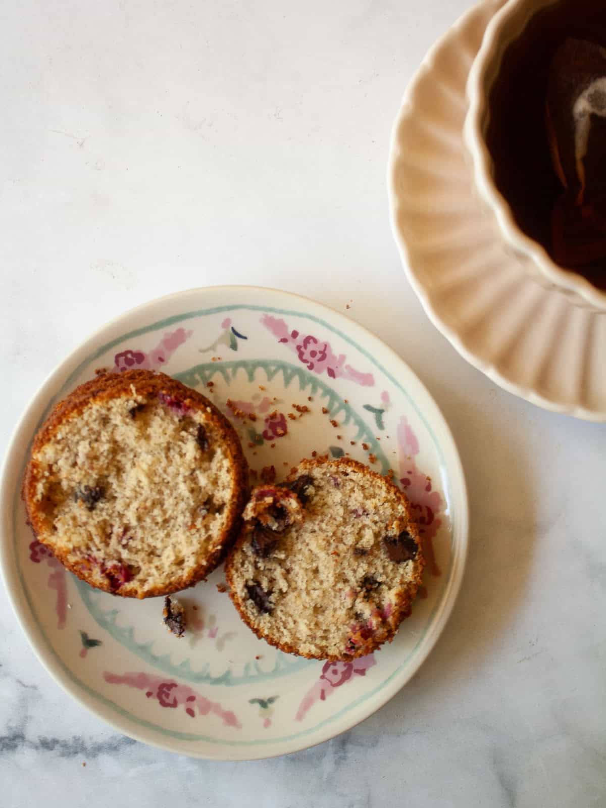A chocolate chip raspberry muffin on a plate and a cup of coffee.