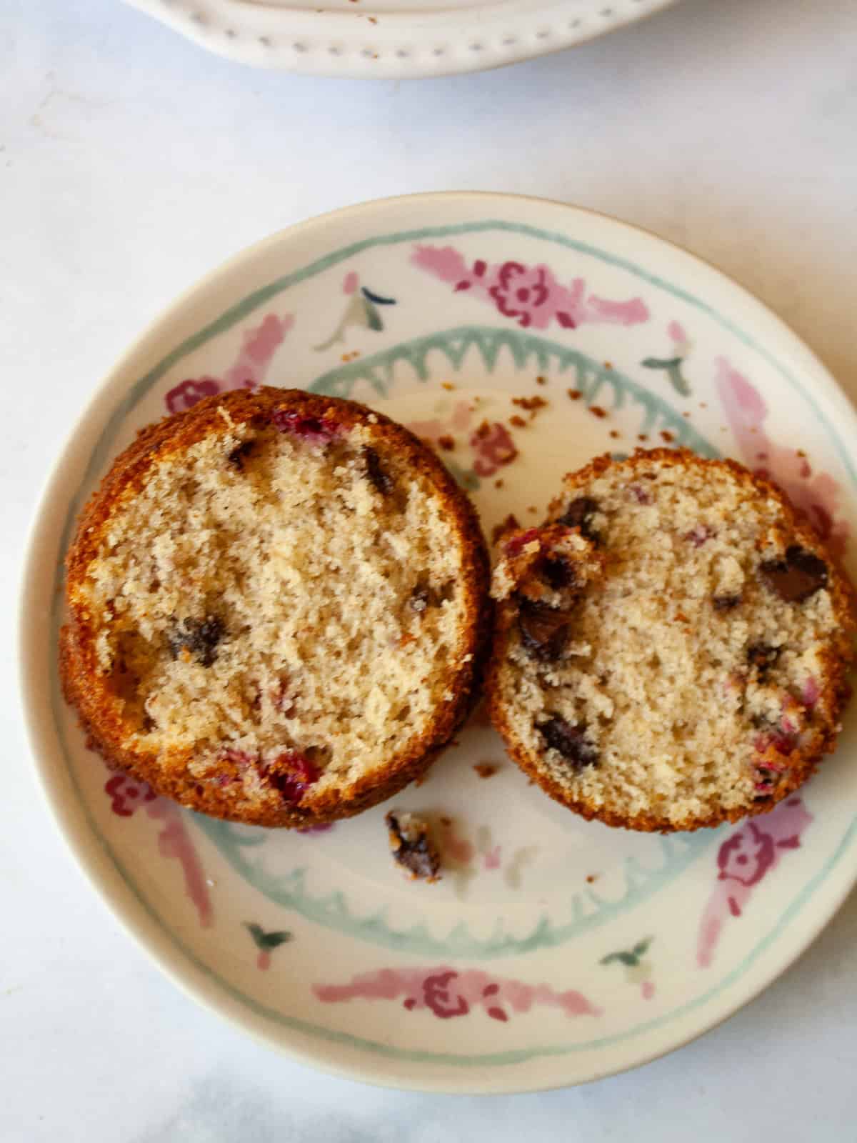 Soft and tender chocolate chip raspberry muffins are made with whole grain flour (easily gluten-free), fruit, and semisweet chocolate! Two halves of a chocolate chip raspberry muffin on a plate.