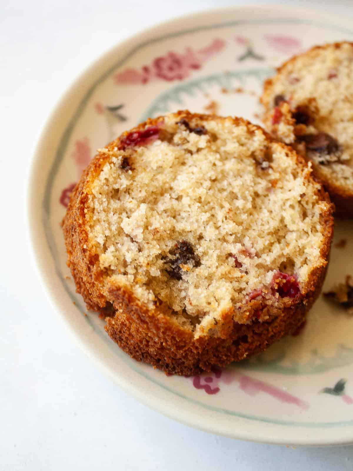 Soft and tender chocolate chip raspberry muffins are made with whole grain flour (easily gluten-free), fruit, and semisweet chocolate! Half of a chocolate chip raspberry muffin on a plate.