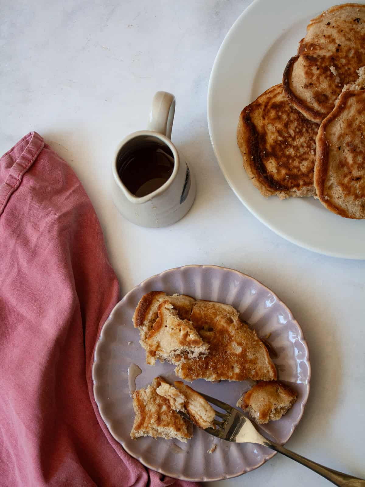 These strawberry pancakes feature fresh, juicy strawberries, whole grain flour, and a light and fluffy crumb. Gluten-free if needed. A strawberry pancake and a fork on a plate, with a napkin and a pitcher of maple syrup.