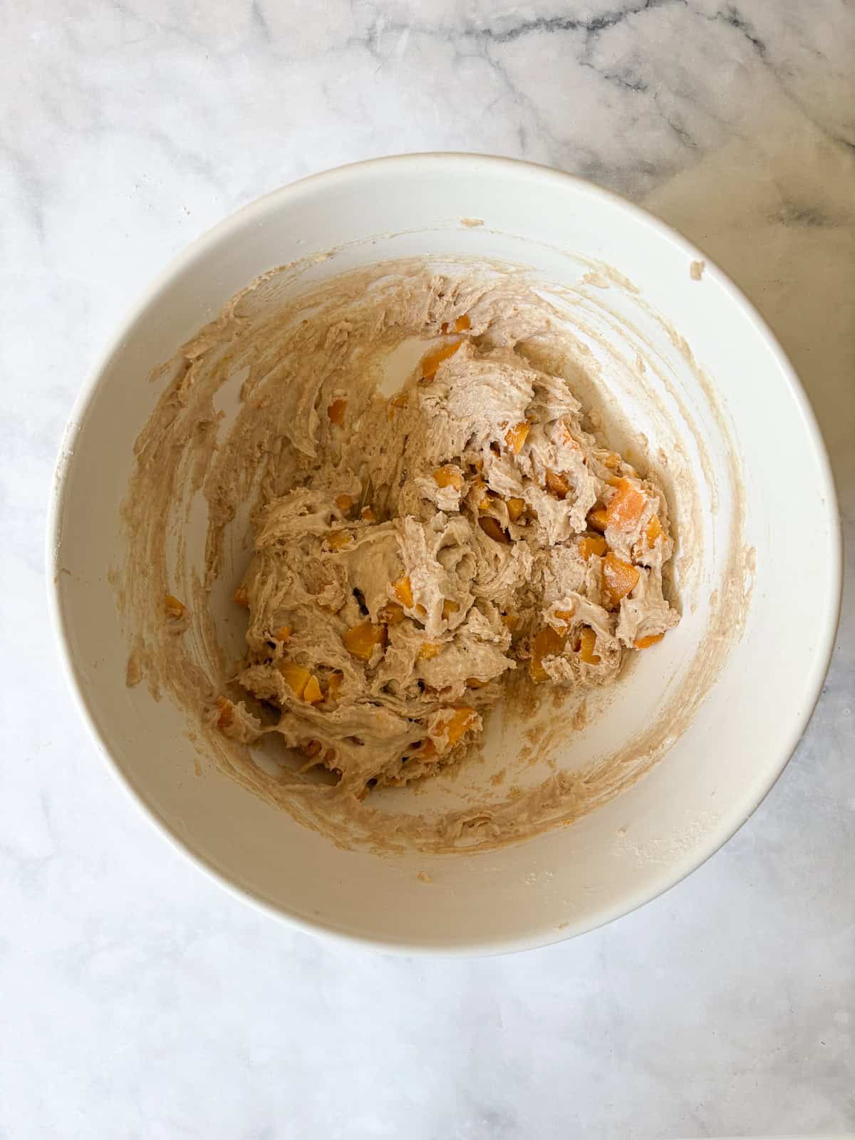 A crisp and cozy oat topping makes this whole grain peach bread shine! Featuring juicy bites of peaches and a brown sugar-cinnamon swirl. Whole grain peach bread batter in a bowl.