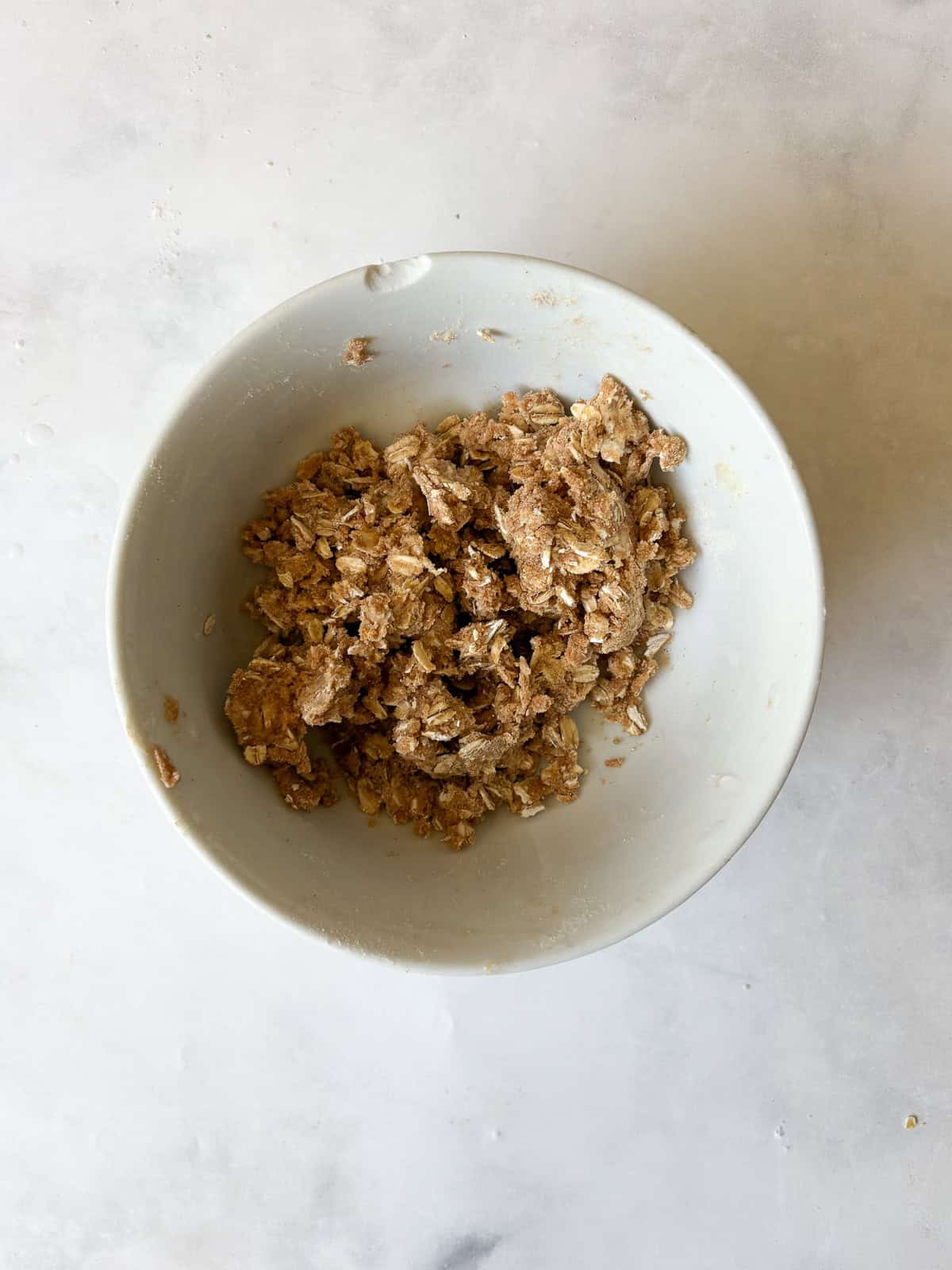 A crisp and cozy oat topping makes this whole grain peach bread shine! Featuring juicy bites of peaches and a brown sugar-cinnamon swirl. The oat topping for whole grain peach bread in a bowl.