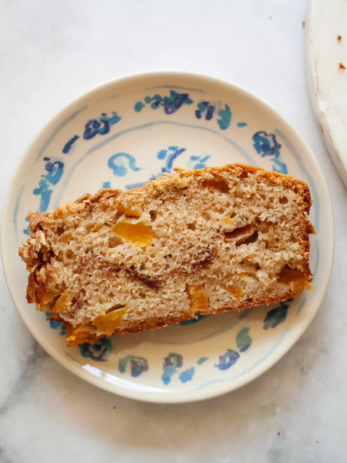A crisp and cozy oat topping makes this whole grain peach bread shine! Featuring juicy bites of peaches and a brown sugar-cinnamon swirl. A slice of whole grain peach bread on a plate.