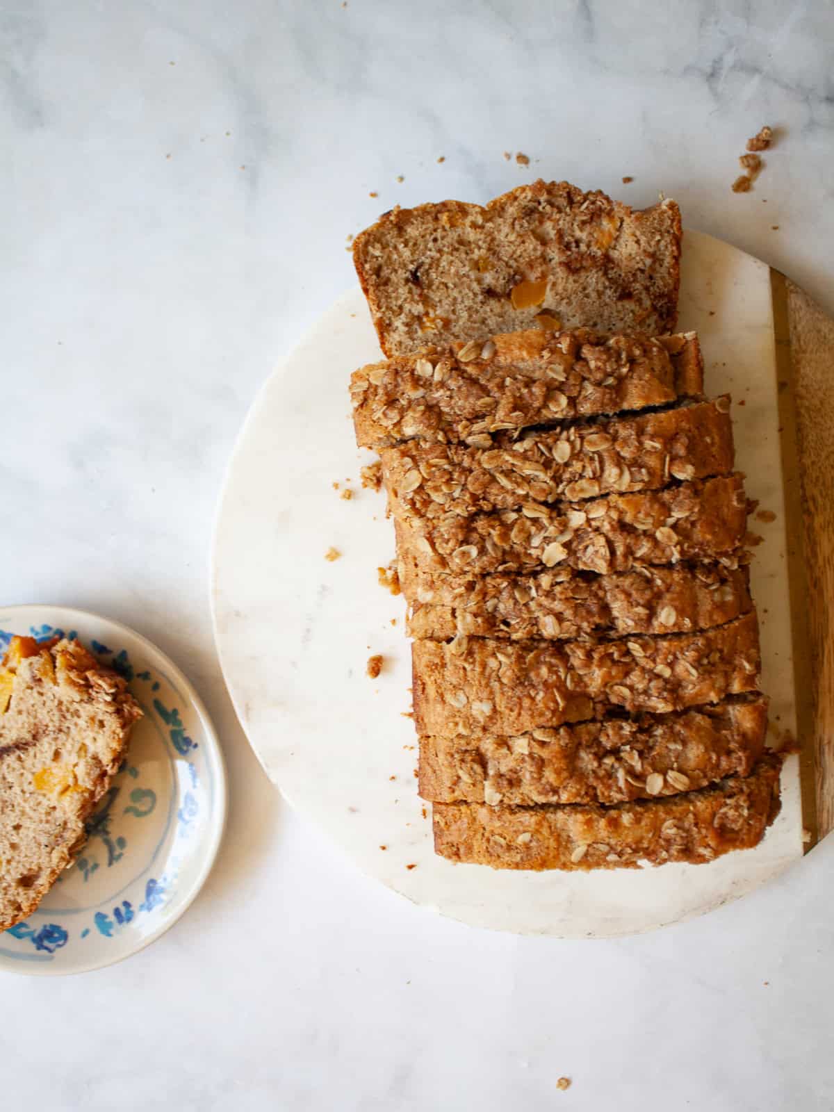 A crisp and cozy oat topping makes this whole grain peach bread shine! Featuring juicy bites of peaches and a brown sugar-cinnamon swirl. A sliced loaf of whole grain peach bread next to a slice on a plate.