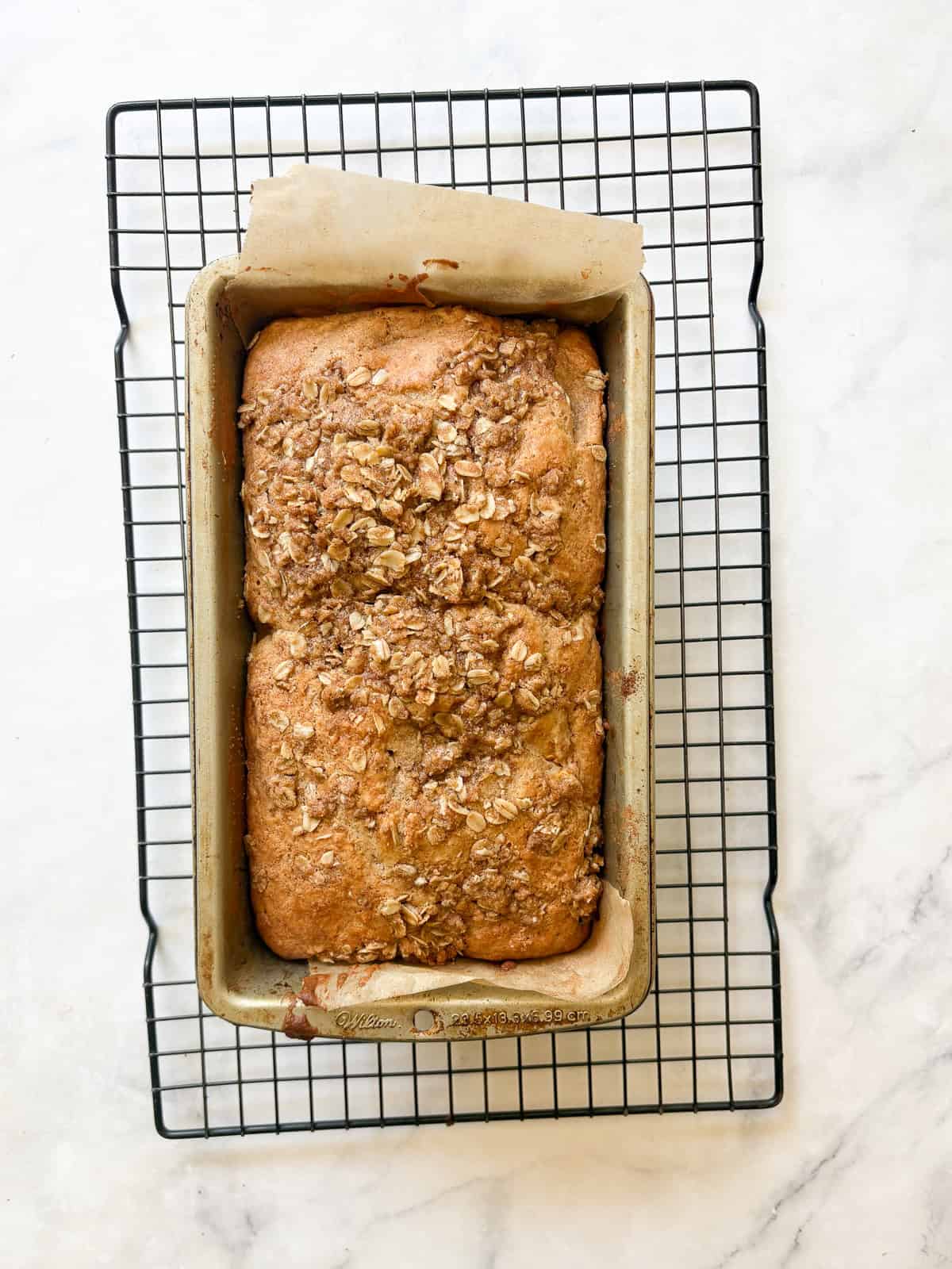 A crisp and cozy oat topping makes this whole grain peach bread shine! Featuring juicy bites of peaches and a brown sugar-cinnamon swirl. A loaf of whole grain peach bread cools on a rack.