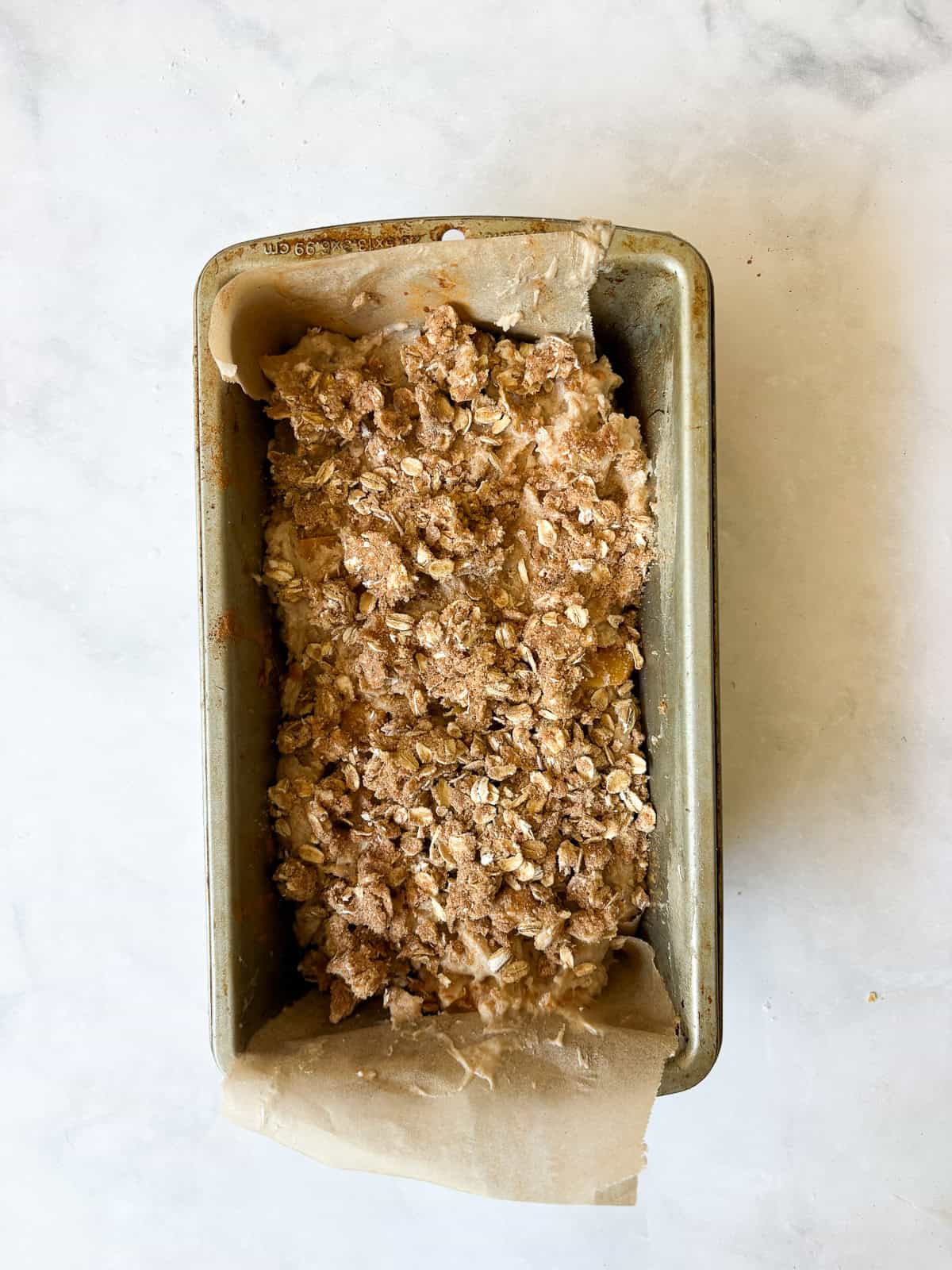 A crisp and cozy oat topping makes this whole grain peach bread shine! Featuring juicy bites of peaches and a brown sugar-cinnamon swirl. Whole grain peach bread with oat topping in a loaf pan.