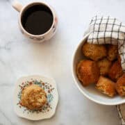A gluten free peach muffin on a plate next to a bowl of muffins.