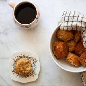 A gluten free peach muffin on a plate next to a bowl of muffins.