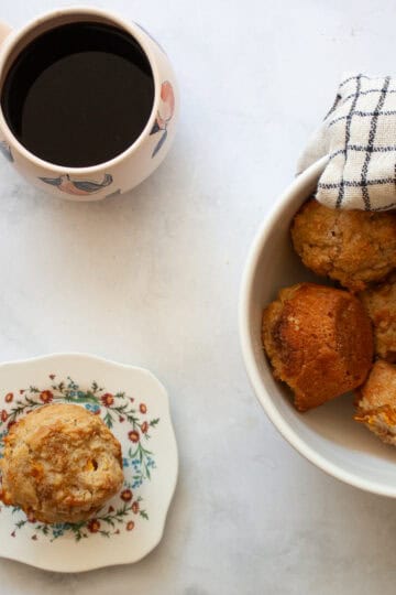 A gluten free peach muffin on a plate next to a bowl of muffins.