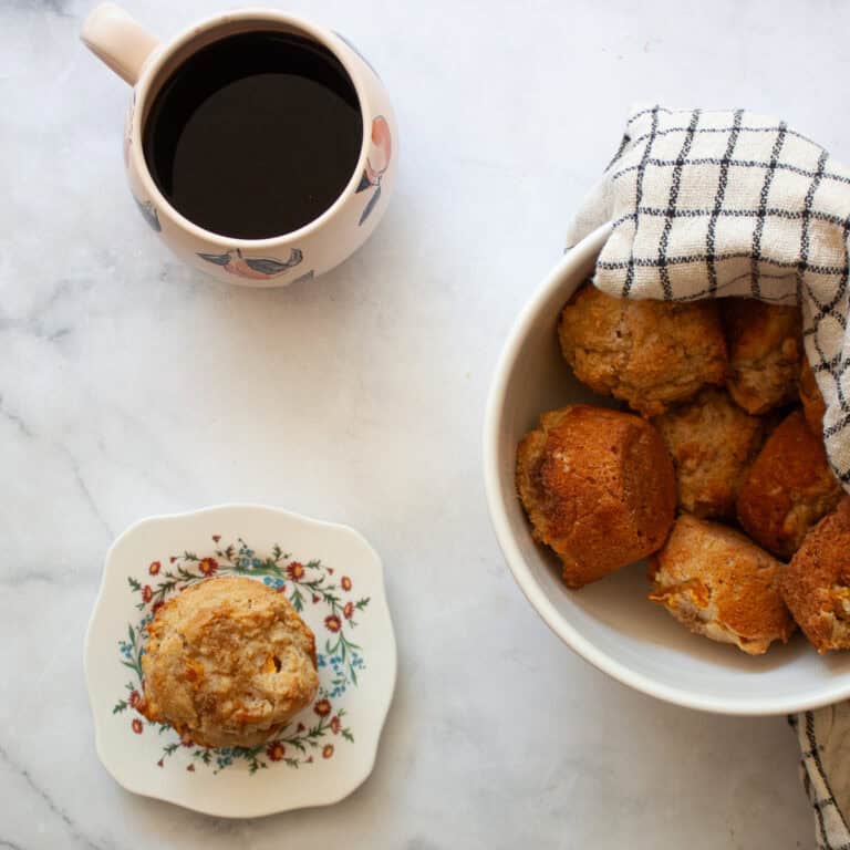 A gluten free peach muffin on a plate next to a bowl of muffins.