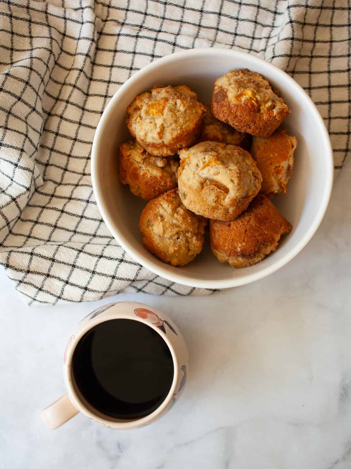 A bowl of gluten free peach muffins and a cup of coffee.