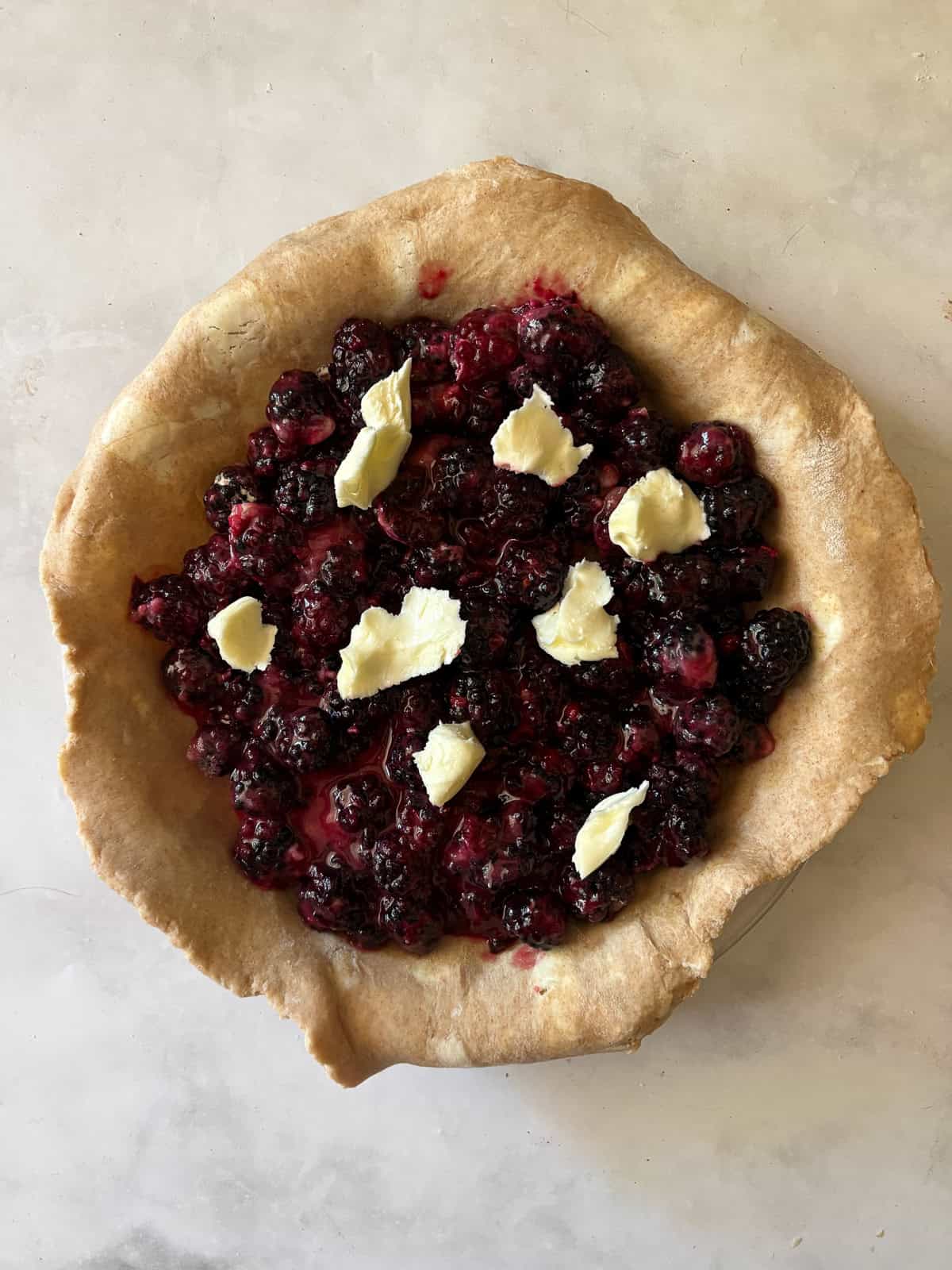 A simple method and ingredients makes this blackberry pie an easy, delicious summer bake. Make gluten-free or not, as needed! Blackberry pie filling is topped with butter in a pie pan.