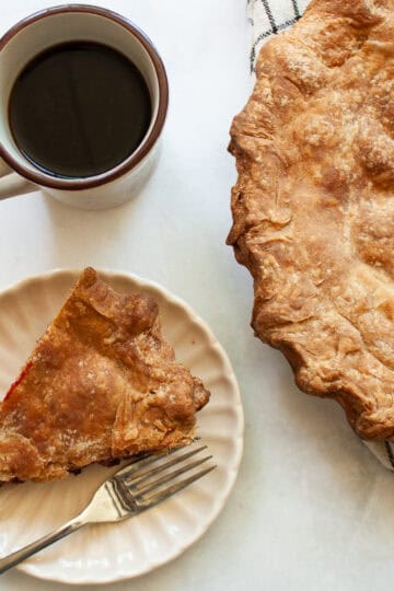 A cup of coffee next to a homemade blackberry pie.