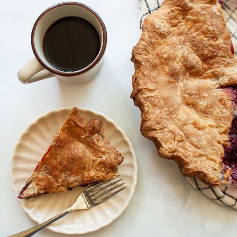 A cup of coffee next to a homemade blackberry pie.