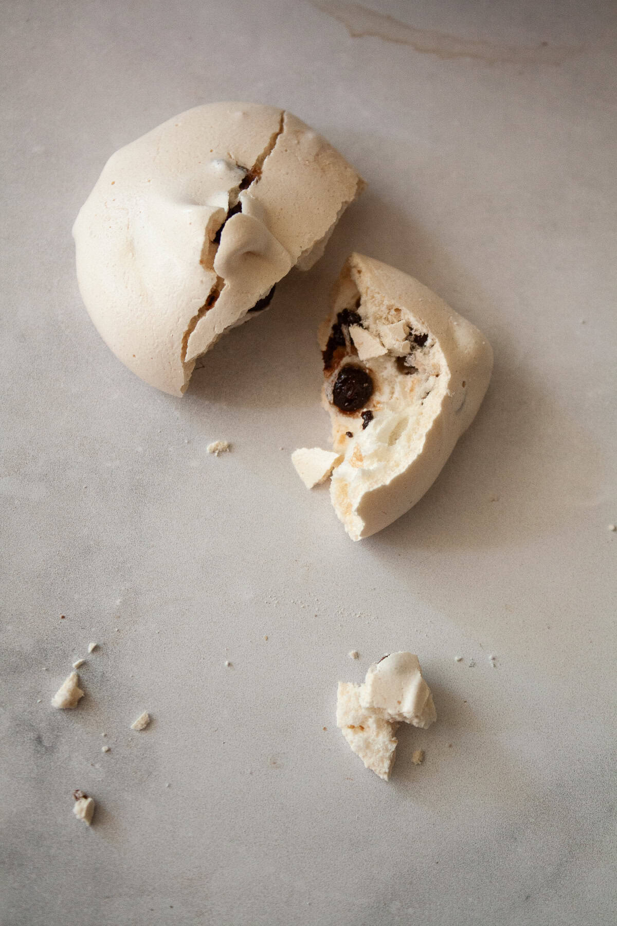 Marshmallowy chocolate chip meringue cookies are studded with mini chocolate chips for bursts of semisweet chocolate in every bite. A chocolate chip meringue cookie broken in half.