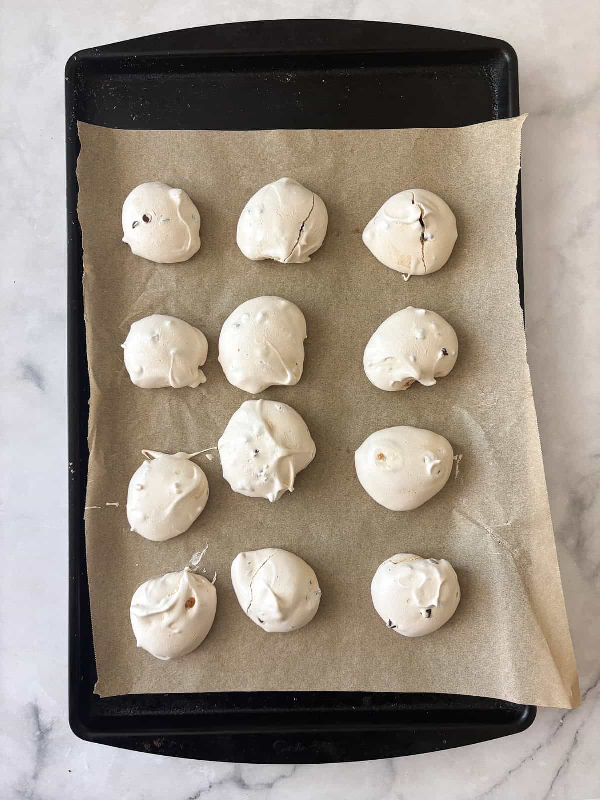 Marshmallowy chocolate chip meringue cookies are studded with mini chocolate chips for bursts of semisweet chocolate in every bite. A tray of baked chocolate chip meringue cookies.