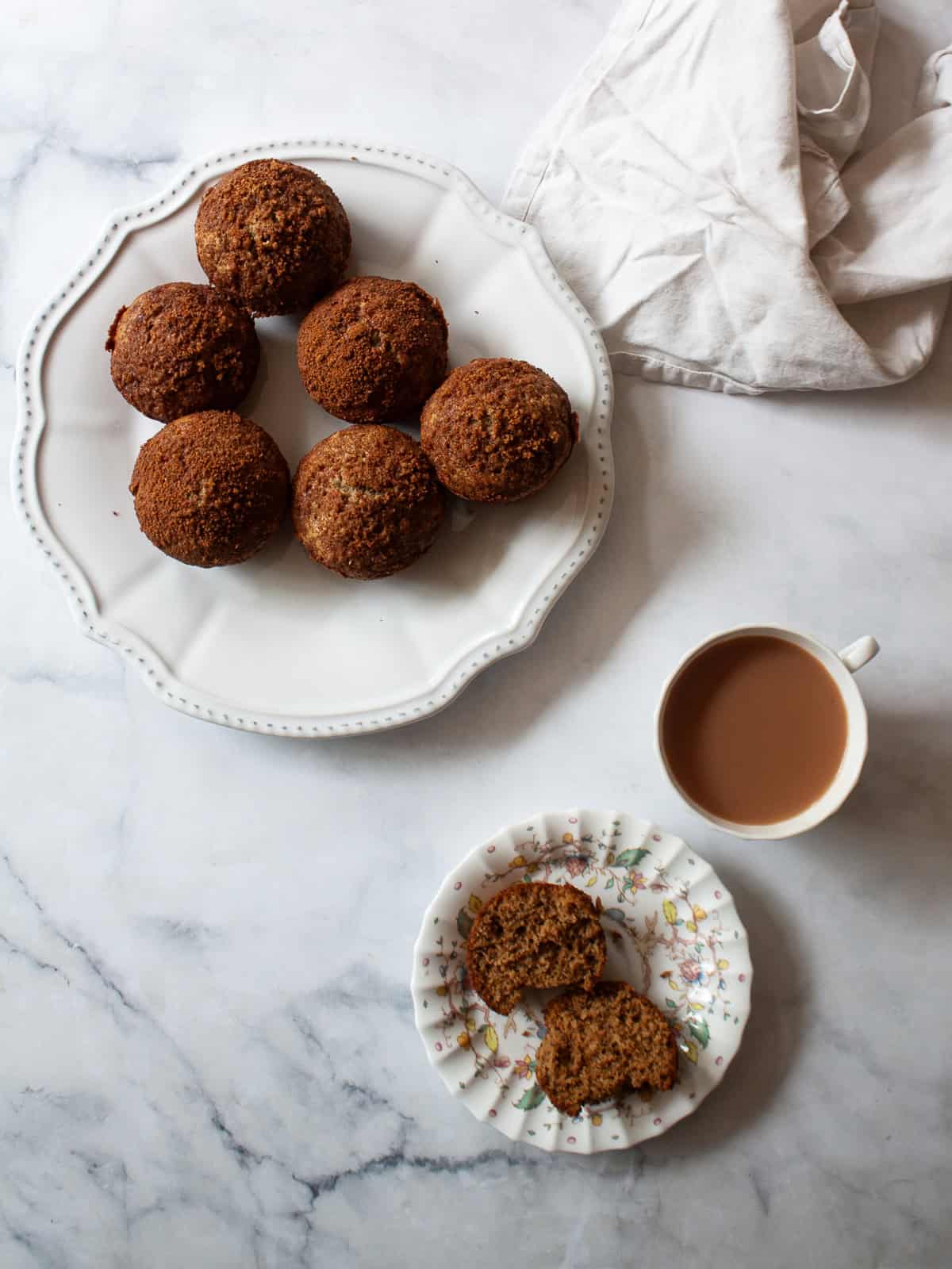 Simple and lightly sweet cinnamon banana muffins are made with wholesome ingredients and finished with a cap of cinnamon and brown sugar. A cup of tea next to cinnamon banana muffins on a plate.