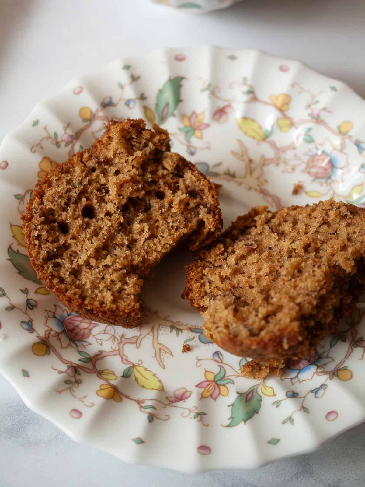Simple and lightly sweet cinnamon banana muffins are made with wholesome ingredients and finished with a cap of cinnamon and brown sugar. A cinnamon banana muffin is cut in half and served on a flowered plate.