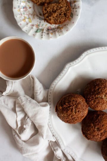 A cup of tea next to cinnamon banana muffins on a plate.