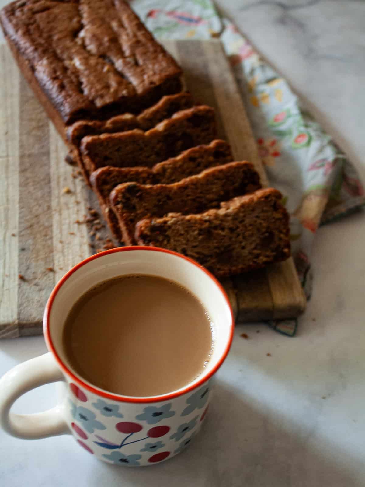 An easy gluten free batter packed with whole grains and yogurt makes for the best loaf of gluten free chocolate chip banana bread. A cup of coffee next to a sliced loaf of gluten free chocolate chip banana bread.