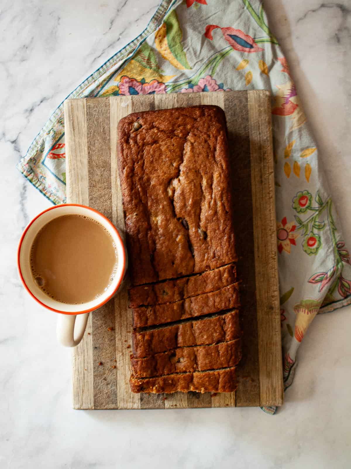 An easy gluten free batter packed with whole grains and yogurt makes for the best loaf of gluten free chocolate chip banana bread. A loaf of gluten free chocolate chip banana bread on a cutting board and a cup of coffee.