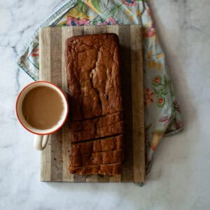 A loaf of gluten free chocolate chip banana bread on a cutting board and a cup of coffee.