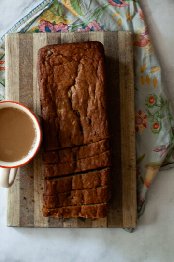 A loaf of gluten free chocolate chip banana bread on a cutting board and a cup of coffee.