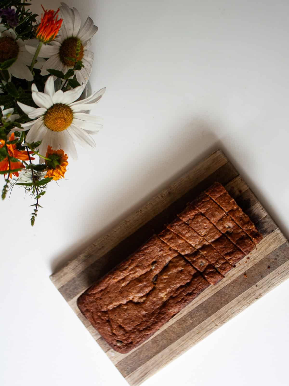An easy gluten free batter packed with whole grains and yogurt makes for the best loaf of gluten free chocolate chip banana bread. Flowers next to a loaf gluten free chocolate chip banana bread.