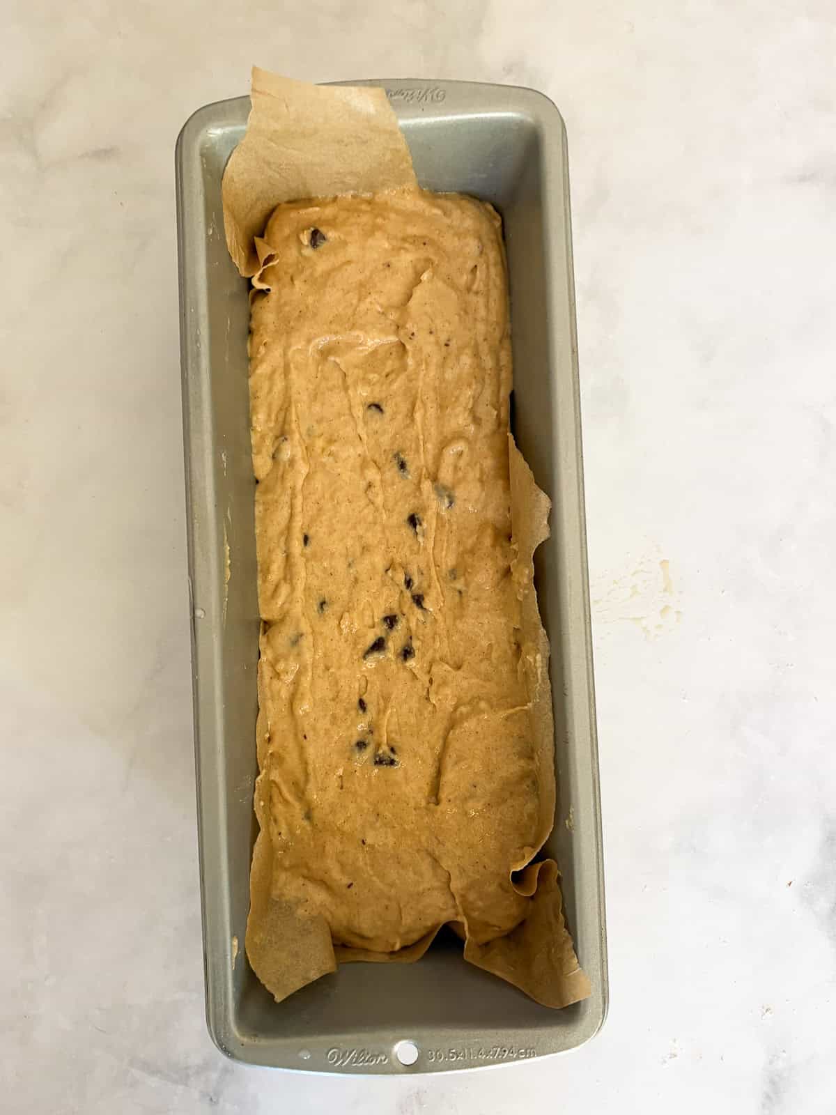 An easy gluten free batter packed with whole grains and yogurt makes for the best loaf of gluten free chocolate chip banana bread. Batter for gluten free chocolate chip banana bread in a loaf pan.