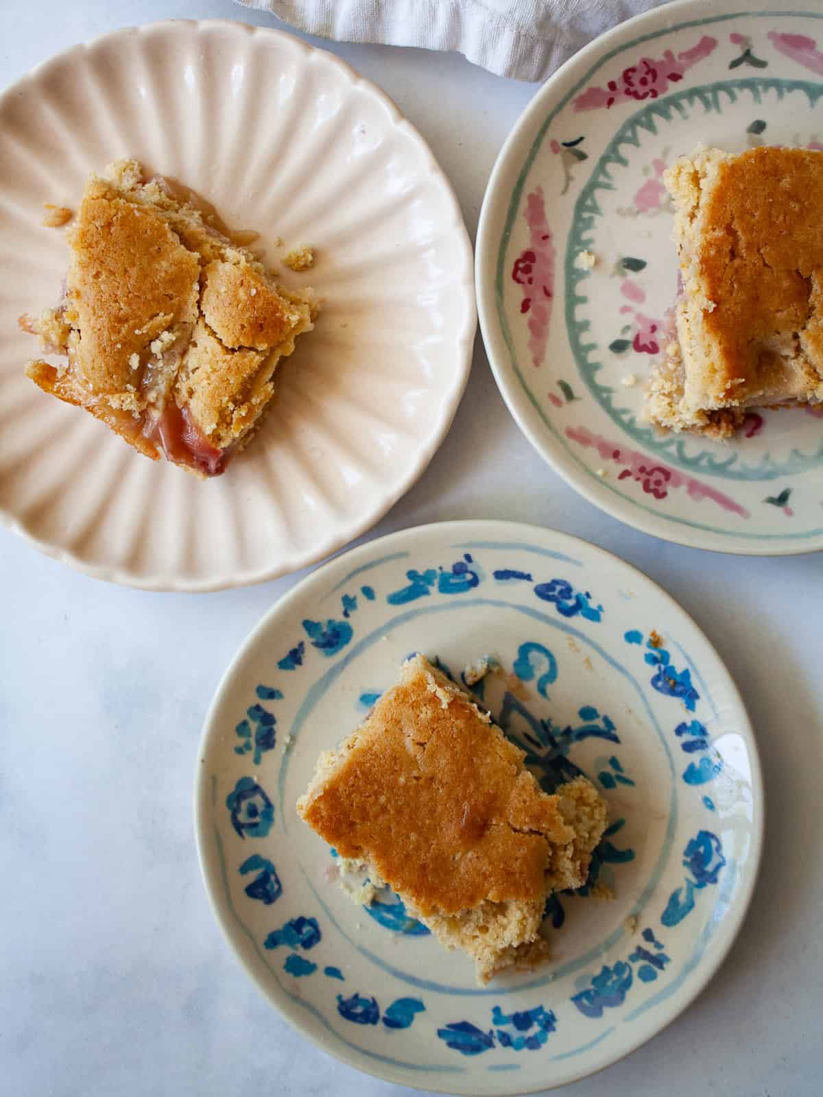 This gluten free peach cobbler features juicy peaches tucked into a pillowy gluten-free batter to make a rustic, simple dessert. Three slices of gluten free peach cobbler on plates.